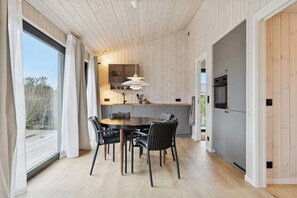A modern kitchen with a dining area, wooden walls, and a large window. - Charming newly built cottage 300 m from beach (Karrebæksminde)