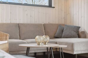 A modern living room with a sectional sofa, a round table, and decorative glass vases. - Charming newly built cottage 300 m from beach (Karrebæksminde)