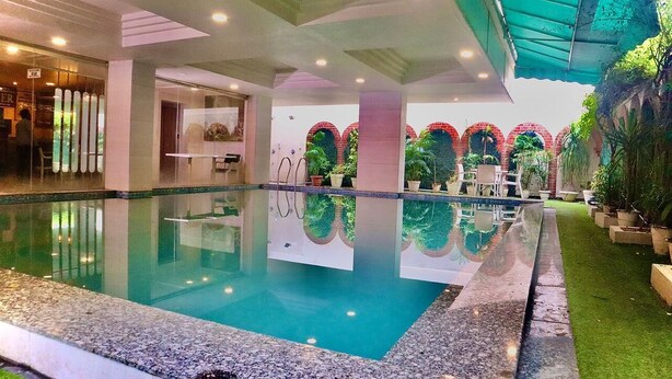 A swimming pool with a glass bottom, surrounded by a covered area with a green canopy. - Hotel Magenta - A unit of Fortune Global (Jaipur)