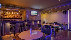 A bar area with stools, tables, and a television screen. - Hotel Magenta - A unit of Fortune Global (Jaipur)