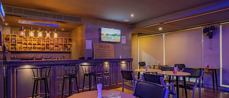 Zona de bar con taburetes, mesas y una pantalla de televisión.