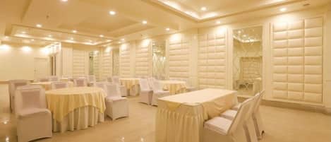 Un salón de banquetes con varias mesas redondas y sillas, techos altos con iluminación empotrada y paneles acolchados en las paredes.