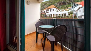 Ein Balkon mit Tisch und zwei Stühlen mit Blick auf eine Hügelkuppe und Gebäude.