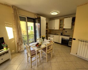 Une cuisine compacte avec des meubles blancs, une table à manger avec des chaises et un petit téléviseur posé sur un meuble.