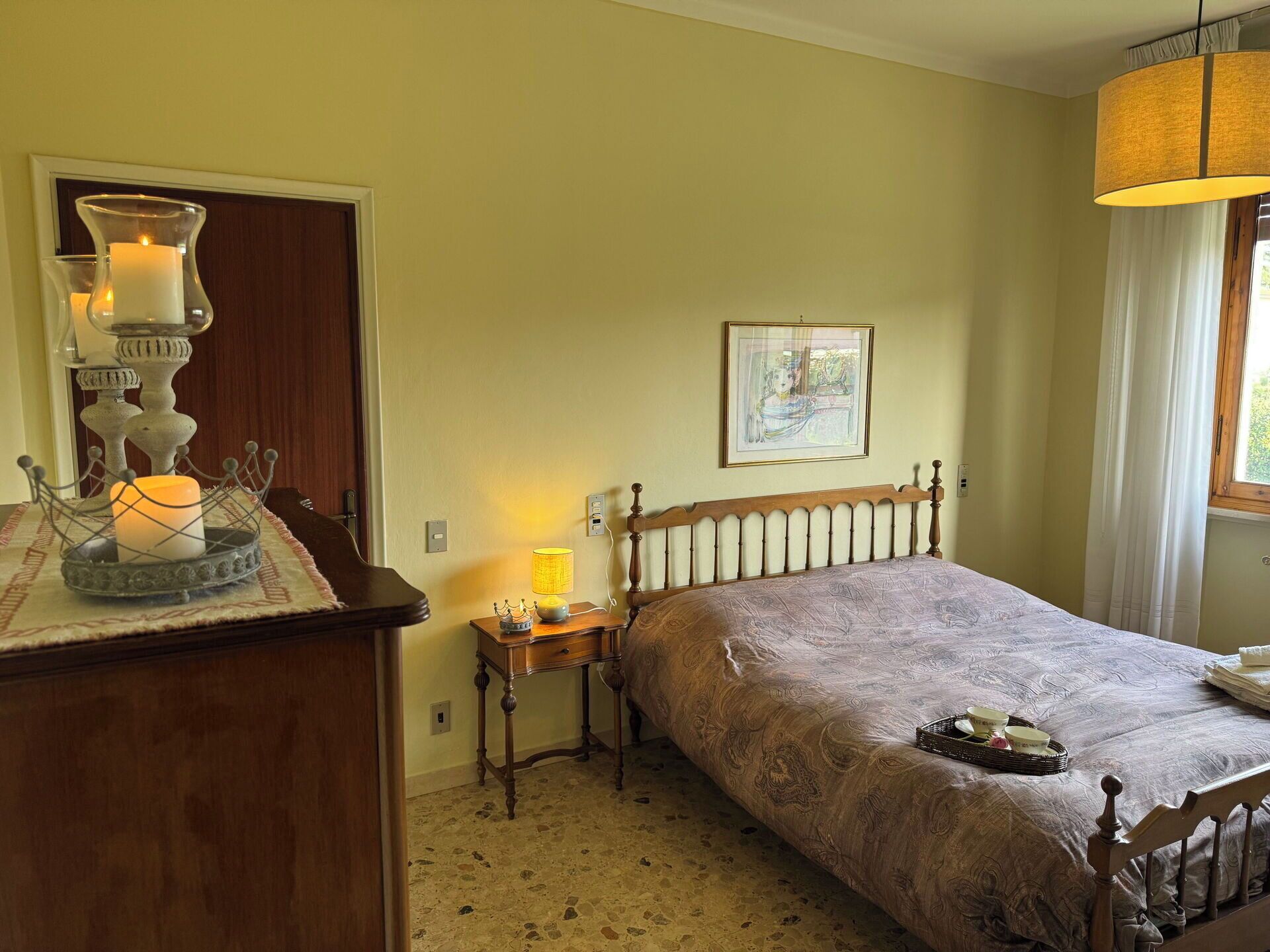 A bedroom with a bed, a nightstand, a lamp, a dresser, and a window with curtains.