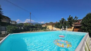 Una piscina rettangolare con acqua cristallina blu, circondata da un bordo bianco e due giochi gonfiabili a galla.
