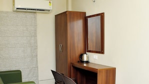 A compact room with a wooden desk, two chairs, a green sofa, a wooden wardrobe, and a wall-mounted air conditioner. - Raj Gharana (Raipur)
