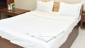 A hotel room with a large bed, a wooden nightstand, a desk, and a chair. - Raj Gharana (Raipur)
