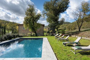 Una piscina con lettini e un edificio in pietra immerso nella campagna.