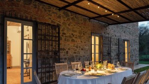 An outdoor dining area with a stone wall, wooden beams, and a table set for a meal. - Country House / Farm House in Olmi with 5 bedrooms sleeps 10 (Olmi)