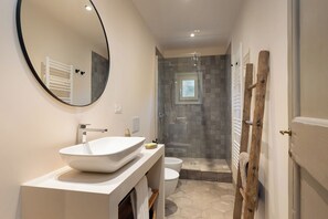 Un bagno moderno con un ampio specchio rotondo, un lavandino bianco, una cabina doccia in vetro e una scala in legno.