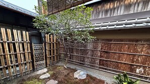 Perinteinen japanilainen puutarha, jossa on bambuaita, pieni puu, askelmakivistä polku ja sammaleen peittämä maa.