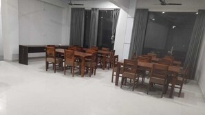 Un vaste espace dédié à la salle à manger, avec de nombreuses tables et chaises en bois, de grandes fenêtres dotées de rideaux et des ventilateurs de plafond.
