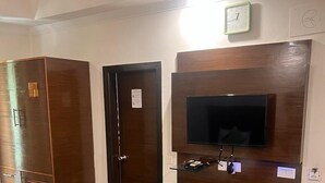 Une pièce avec une armoire en bois, une porte, un téléviseur fixé au mur et un petit banc.