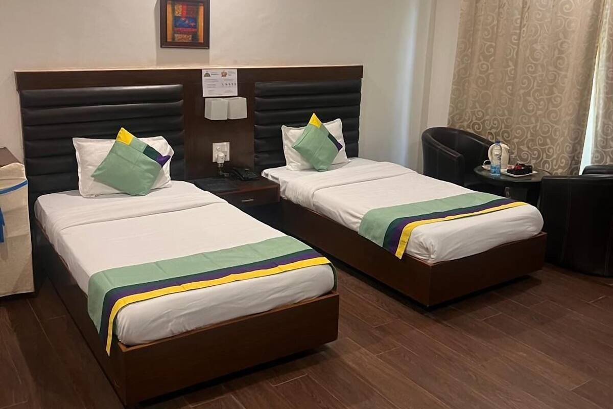 Een hotelkamer met twee bedden, een plafondventilator, een nachtkastje met een lamp en een raam met gordijnen.