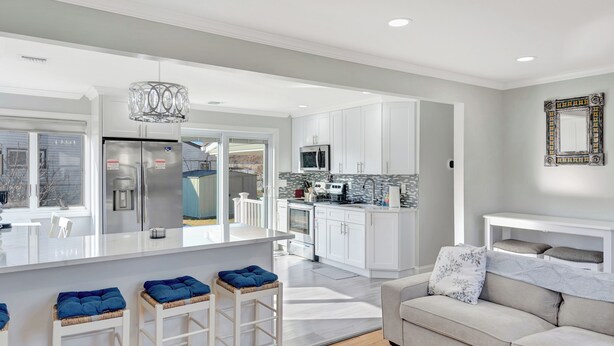 A modern kitchen with white cabinets, a stainless steel refrigerator, and a large island with stools.