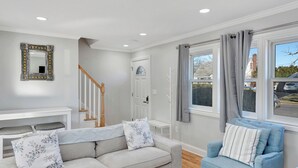 A living room with a grey sofa, a blue armchair, a white bench, a mirror, and a staircase.