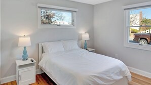 A bedroom with a bed, two bedside tables with lamps, a window with a view of a tree and a vehicle, and a white wardrobe.