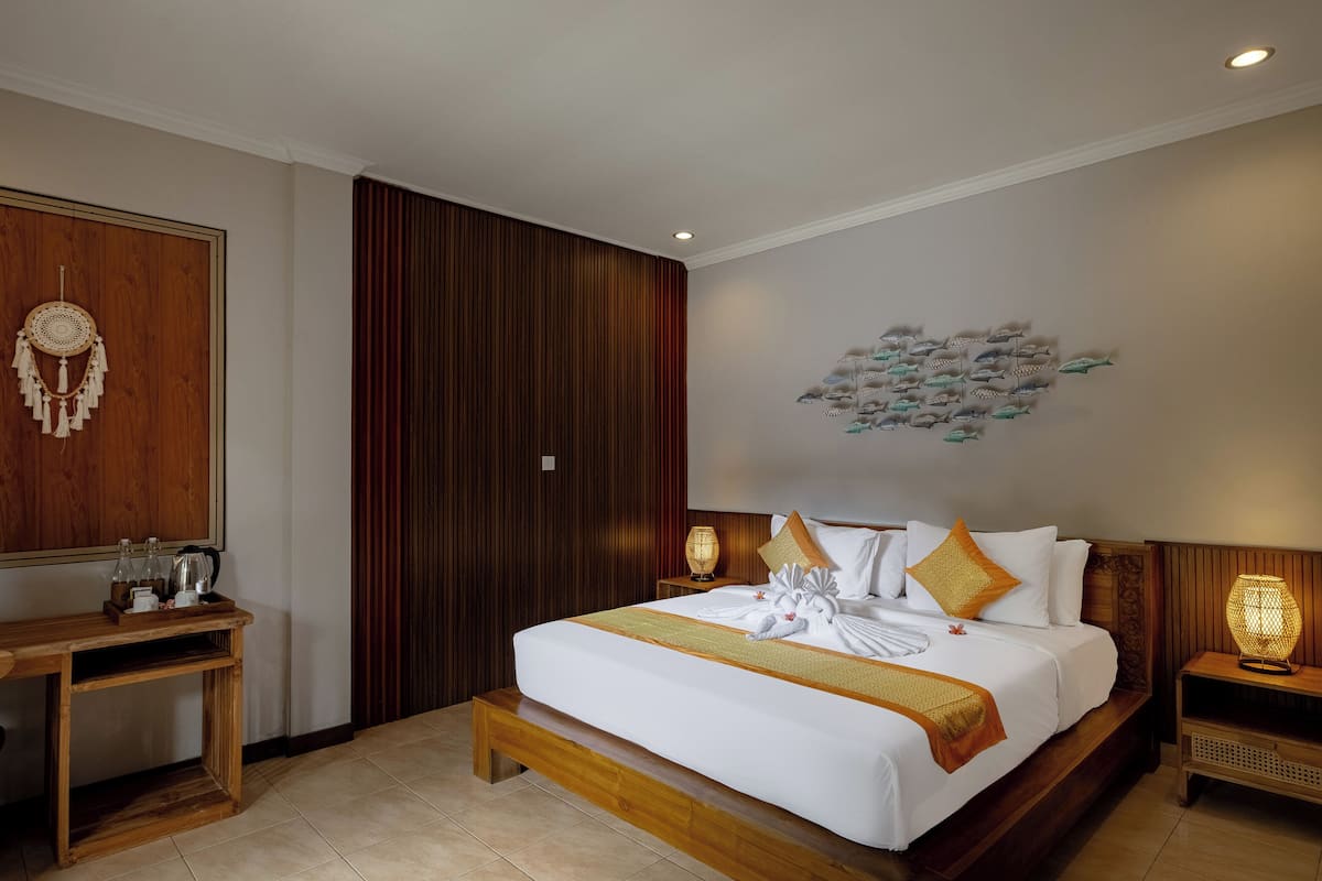 Una habitación de hotel ordenada con una cama grande, una mesita de noche de madera, un escritorio y una obra de arte colgada en la pared.