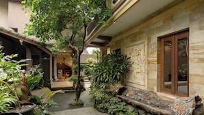 A courtyard with a stone bench, potted plants, and a wooden door. - Togog Polos Ubud House (Ubud)