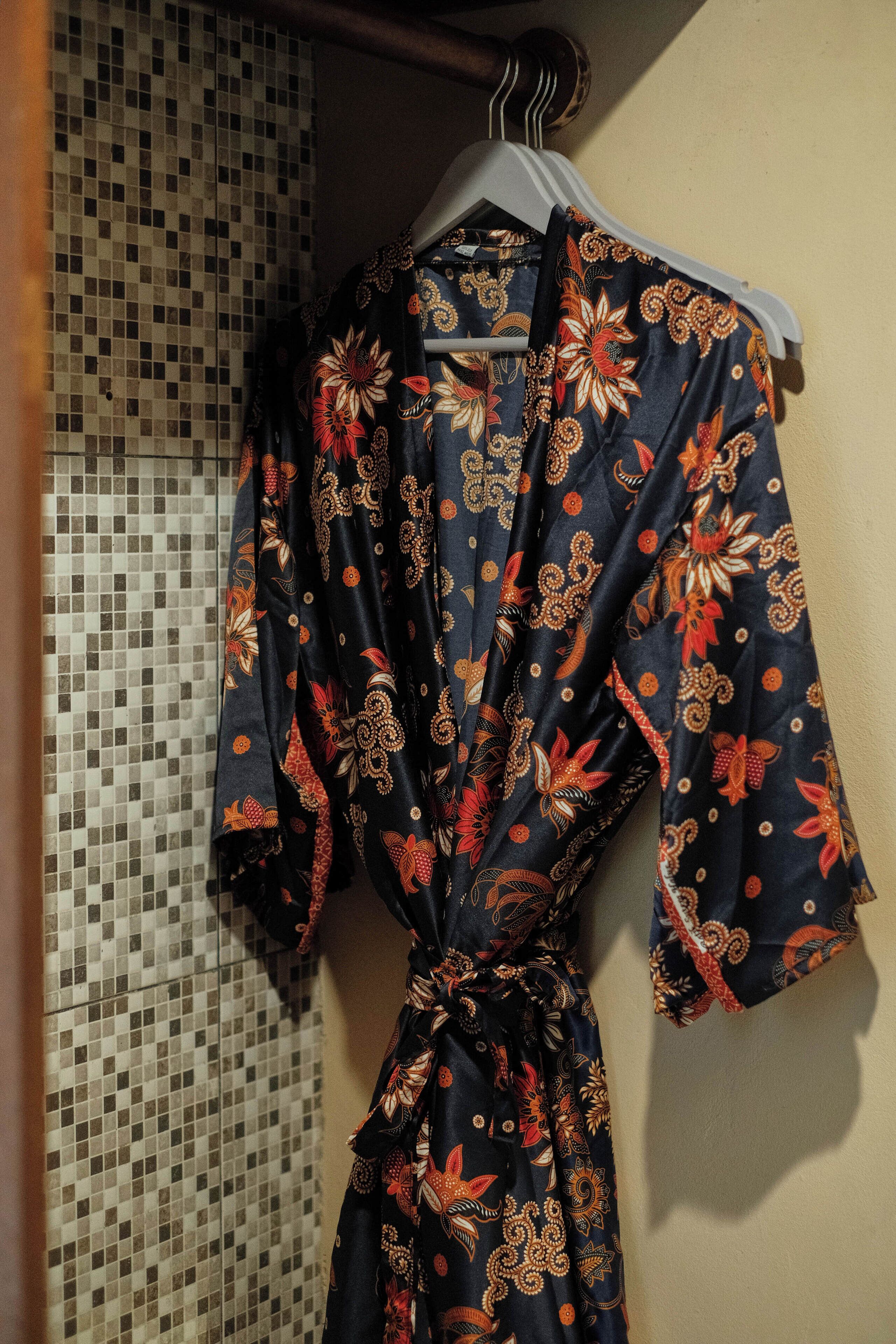 Une longue robe sombre, ornée de motifs floraux, est suspendue à un portant.