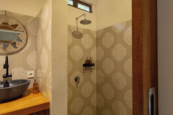 A bathroom with a stone sink, a mirror, a shower with a handheld showerhead, and patterned wallpaper. - Togog Polos Ubud House (Ubud)