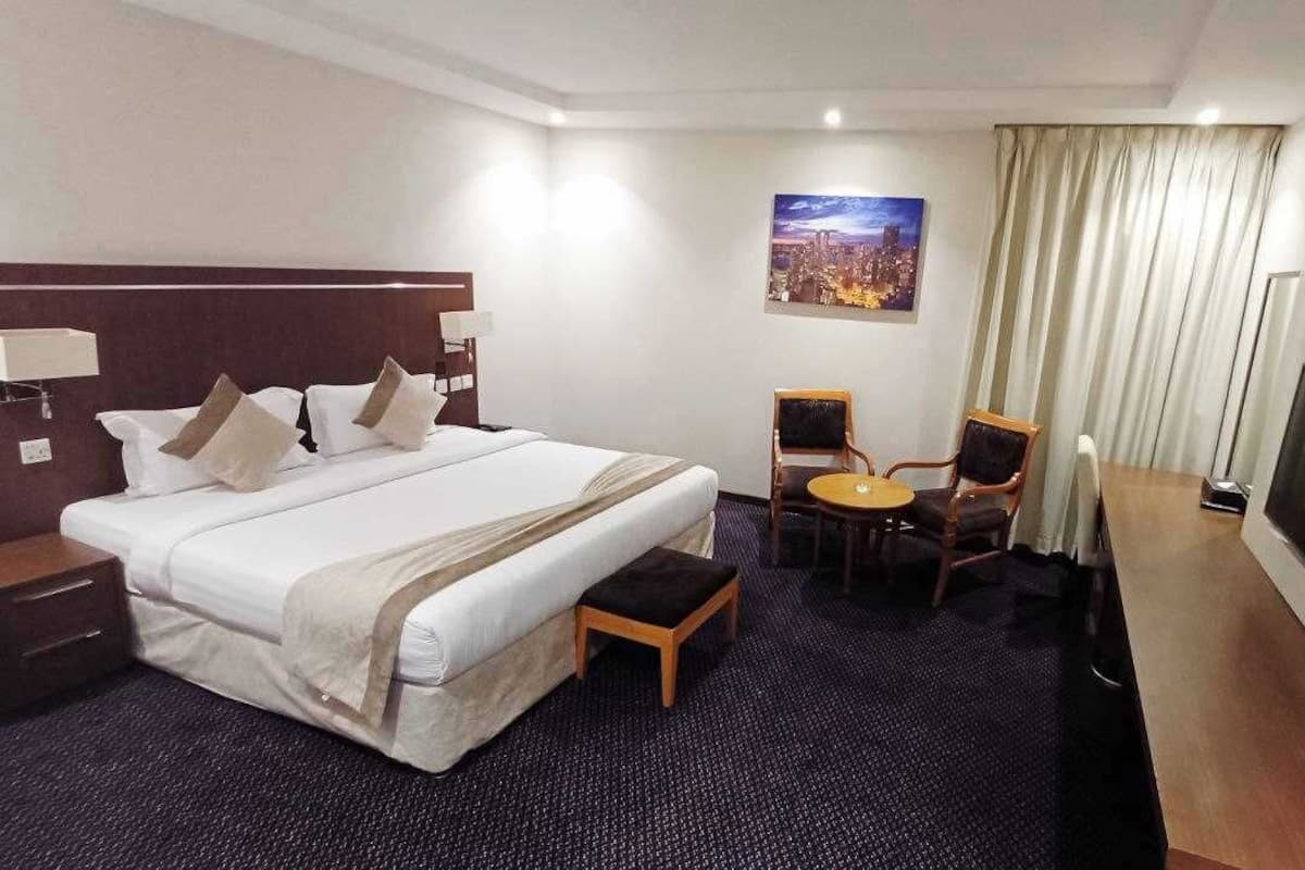 A hotel room with a large bed, a desk with a chair, a television, and a cityscape painting on the wall.