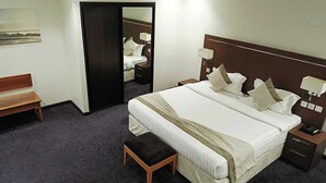 Una camera d'albergo con un letto grande, comodini, una panca e uno specchio.