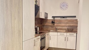 A compact kitchen with wooden flooring, white cabinetry, a built-in oven, a microwave, and a clock on the wall. - Cozy high-quality furnished apartment (Wiesbaden)
