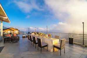 An outdoor dining area with a long table, chairs, and a view of the ocean. - amã Stays & Trails Soul Storries, Mussoorrie (Mussoorie)
