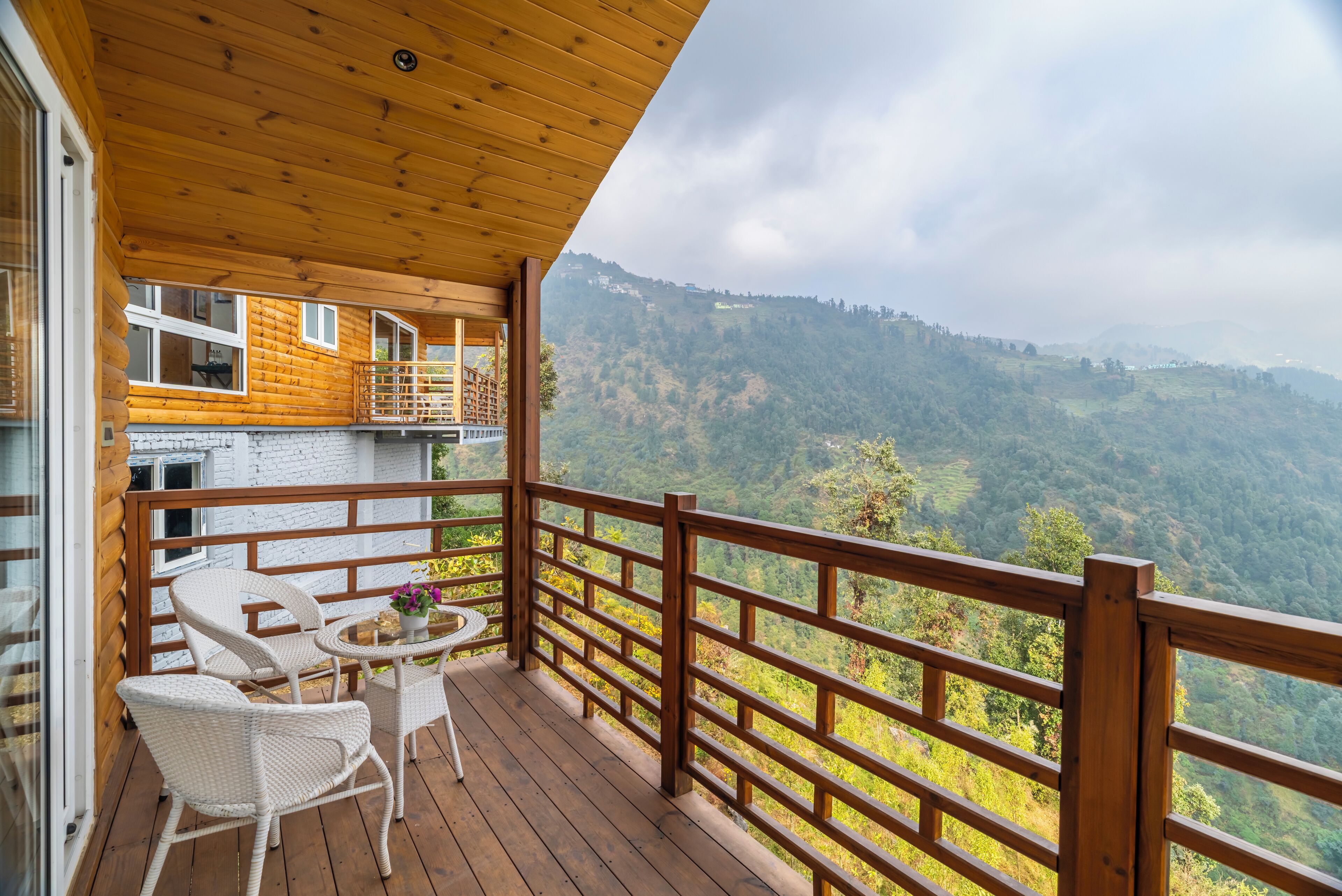 A wooden deck with wicker chairs and a small table, overlooking a mountainous landscape.