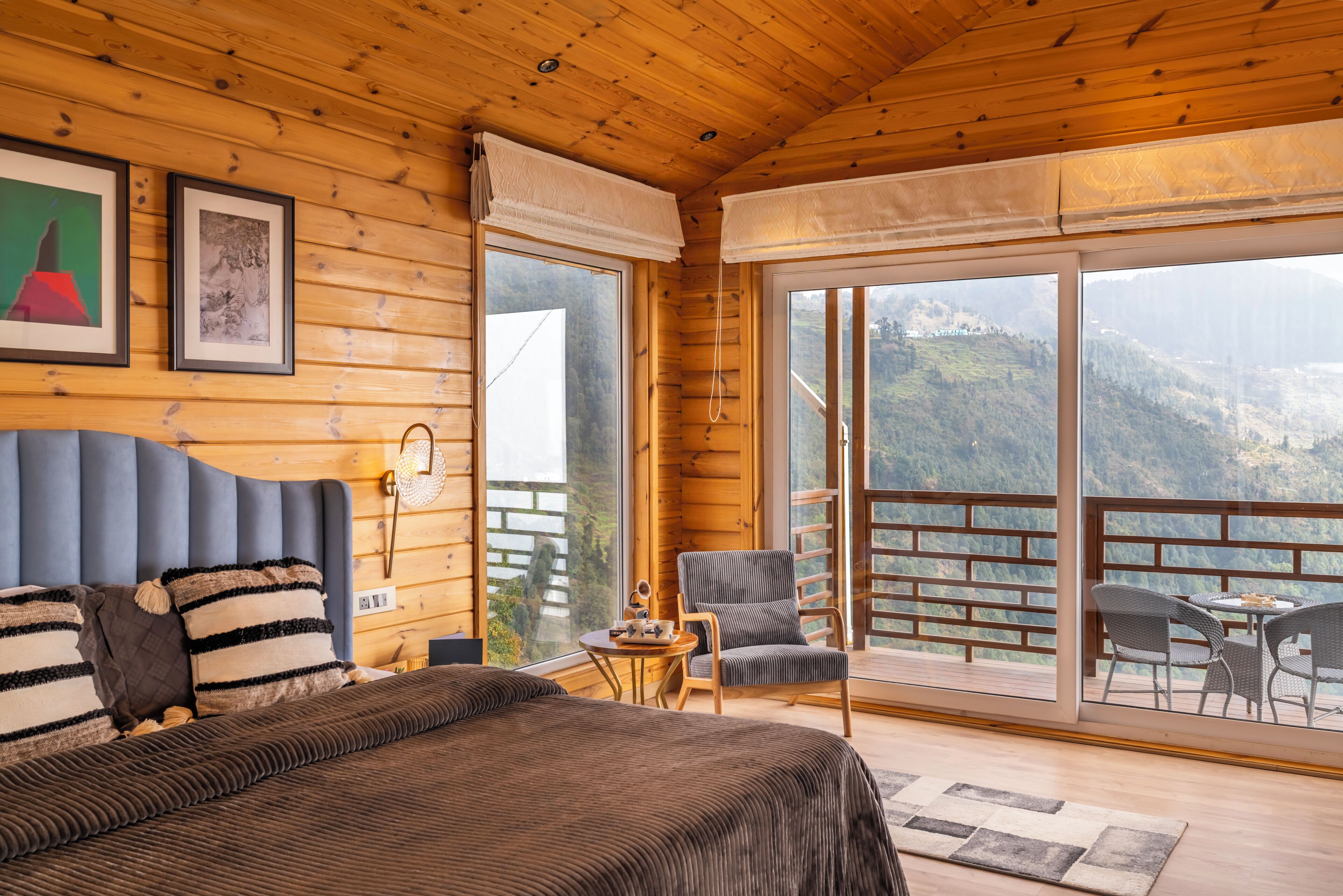 Habitación de cabaña de madera con cama, una silla y balcón con vista a las montañas.