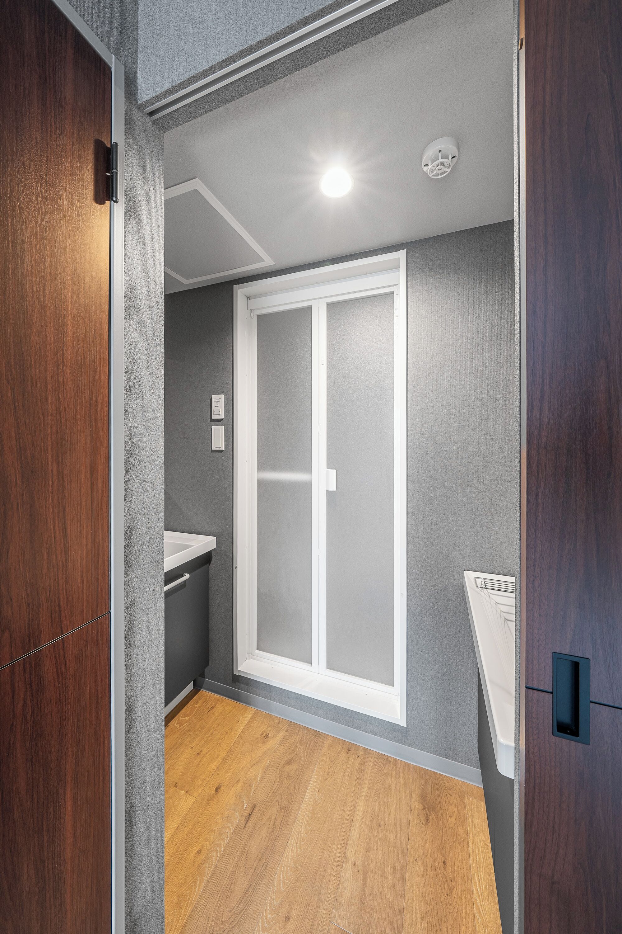 A narrow hallway with a wooden door on the left, a white-framed sliding door on the right, and a small white shelf.