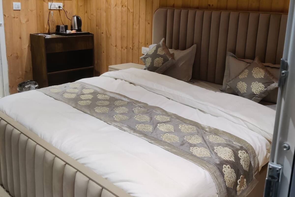 A bedroom with a wooden paneled wall, a flat-screen TV mounted above a wooden nightstand, a bed with a beige headboard and patterned bedspread, and a decorative wall piece above the bed.