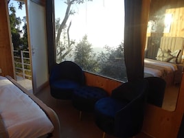 Un dormitorio con un ventanal grande, una cama, dos sillas azules y suelo de madera.