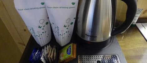 A stainless steel coffee pot, two paper cups with a green design, a pack of tissues, and a box of Nescafe Classic coffee on a black tray.