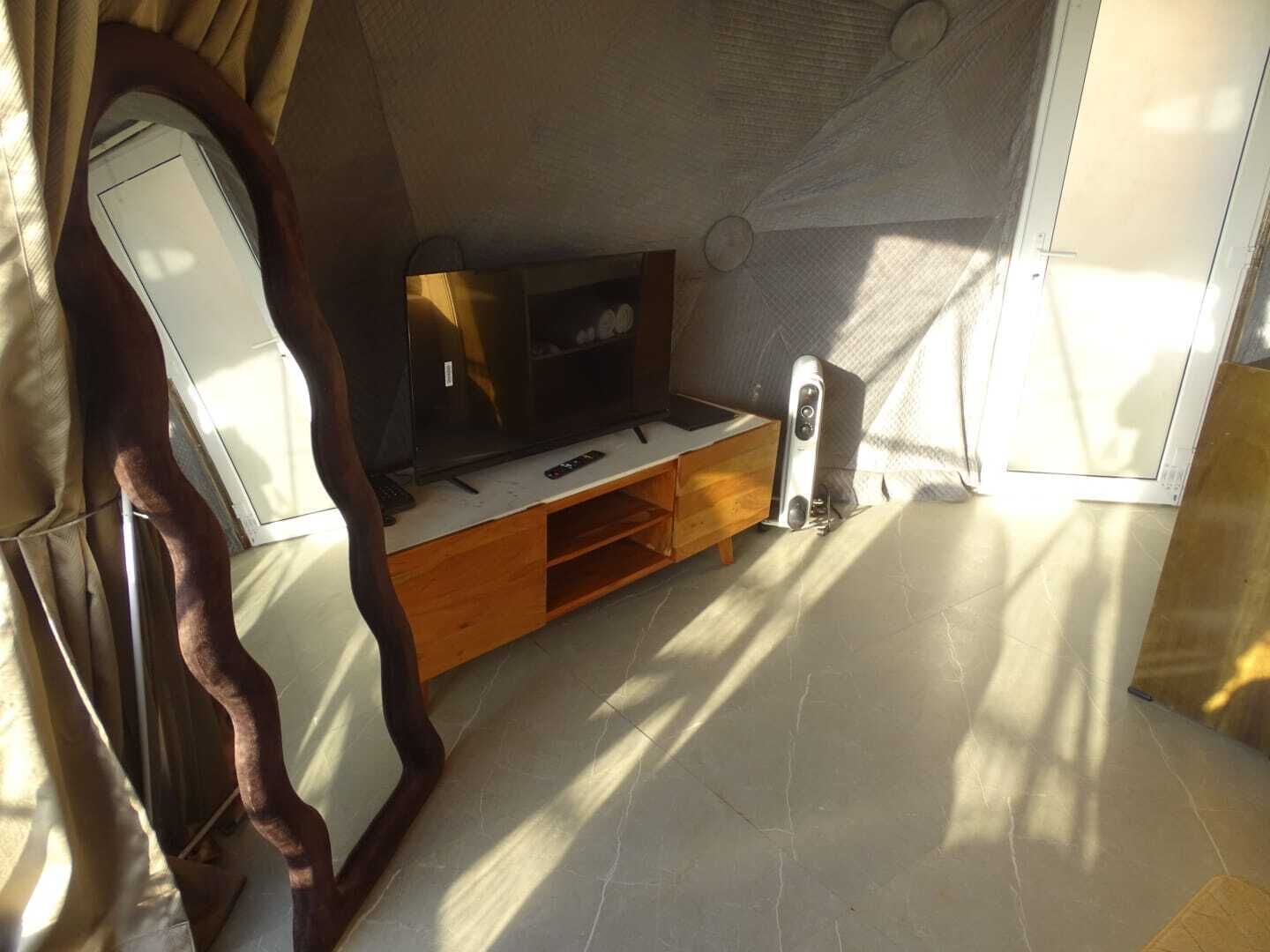 A compact living space with a flat-screen TV, wooden storage unit, and a mirror.