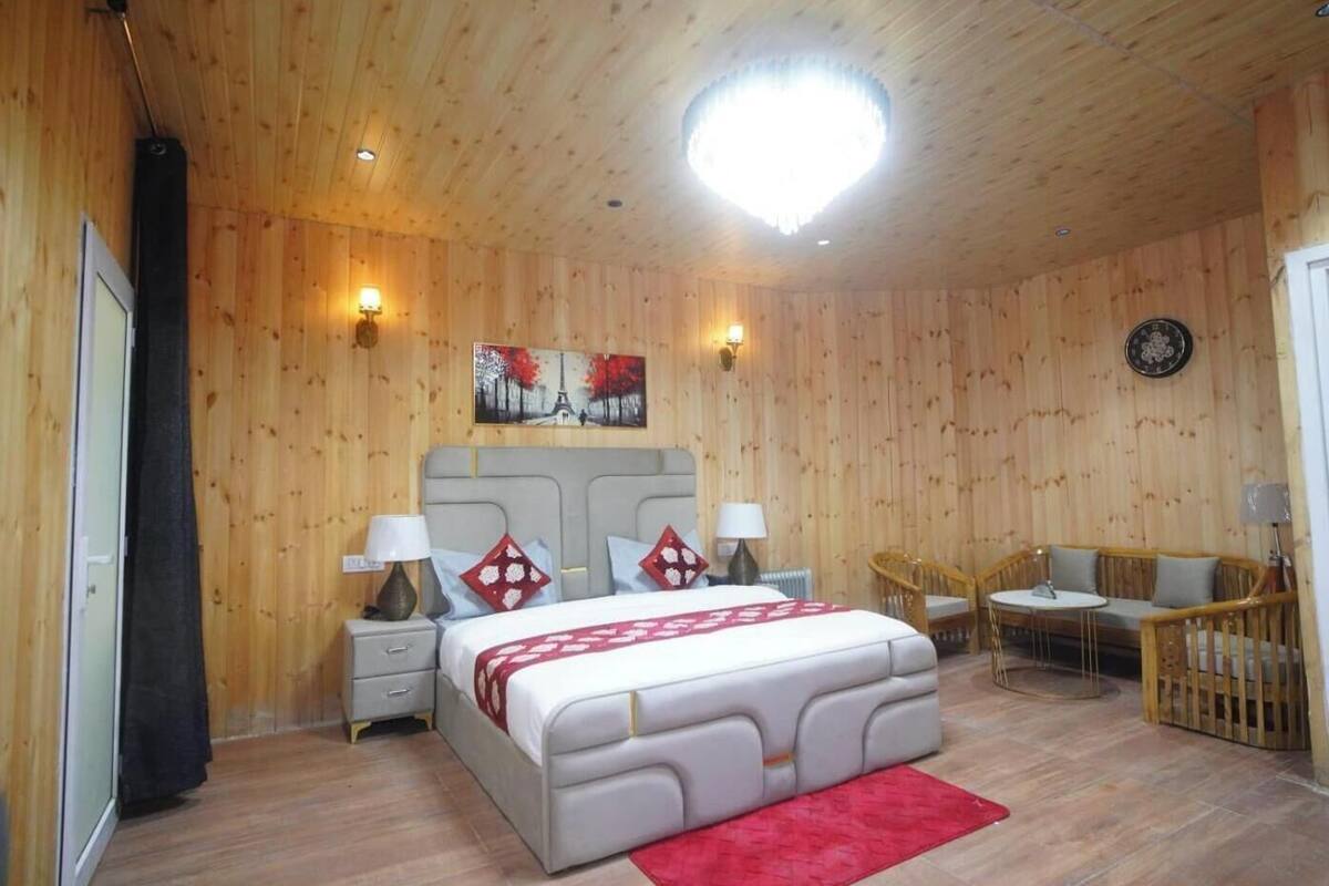 A wooden-paneled room with a bed, bedside tables, a chair, a small table, and a round table.