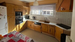 Eine Küche mit Holzausstattung, einem Kühlschrank, einem Backofen, einer Spüle und einem Fenster mit Jalousien.