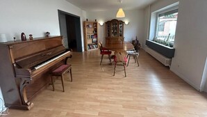 Ein geräumiger Raum mit einem Flügel, einer Holzvitrine und einem großen Fenster, das für natürliches Licht sorgt.