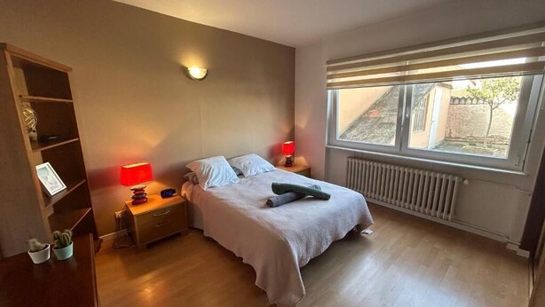 Ein Schlafzimmer mit einem Bett, Nachttischen, einem Fenster und einer Heizung.