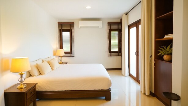 A bedroom with a large bed, two bedside tables with lamps, a wardrobe, and a potted plant. - Amazing 3-bedroom house in charming Mae Rim, Chiangmai (Tambon Rim Tai)