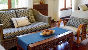 A room with a sofa, a dining table with a blue tablecloth, and a bed. There is a window with curtains, a potted plant, and a framed picture on the wall. - Amazing 3-bedroom house in charming Mae Rim, Chiangmai (Tambon Rim Tai)