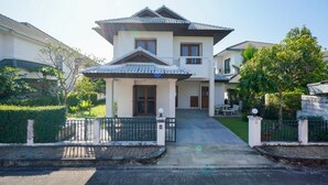 A two-story house with a tiled roof, a front porch, and a gated driveway. - Amazing 3-bedroom house in charming Mae Rim, Chiangmai (Tambon Rim Tai)