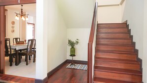 A wooden staircase with a handrail, a dining area with a table and chairs, and a hanging light fixture. - Amazing 3-bedroom house in charming Mae Rim, Chiangmai (Tambon Rim Tai)