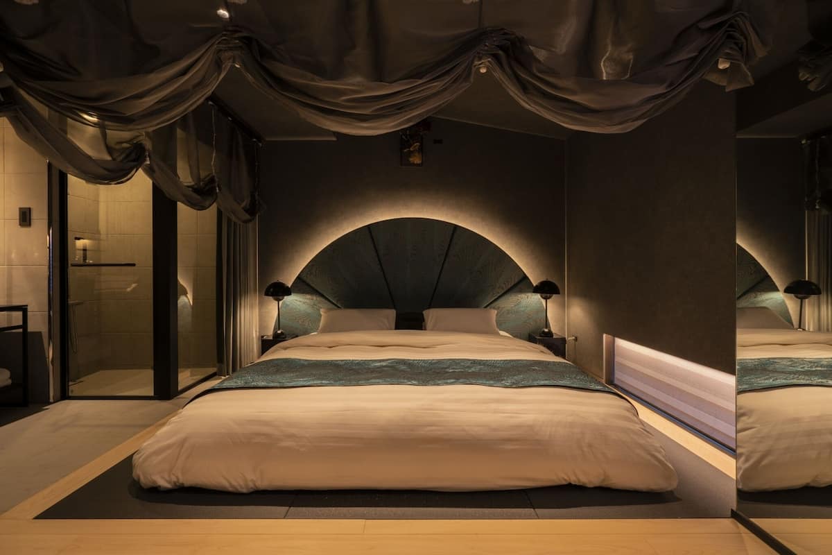 A modern bedroom with a large bed, a glass shower enclosure, and a dark ceiling with draped fabric.