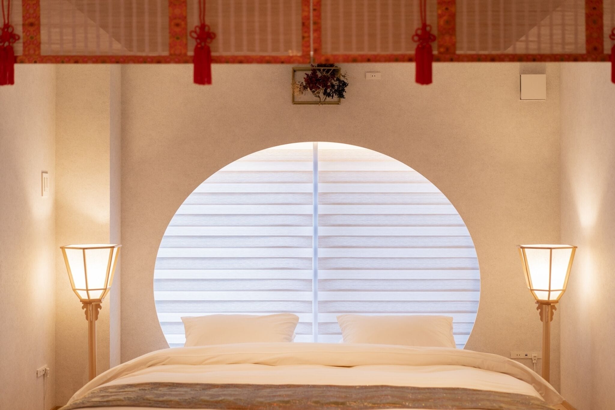 A bedroom with a large arched window, two bedside lamps, and a bed with white bedding.