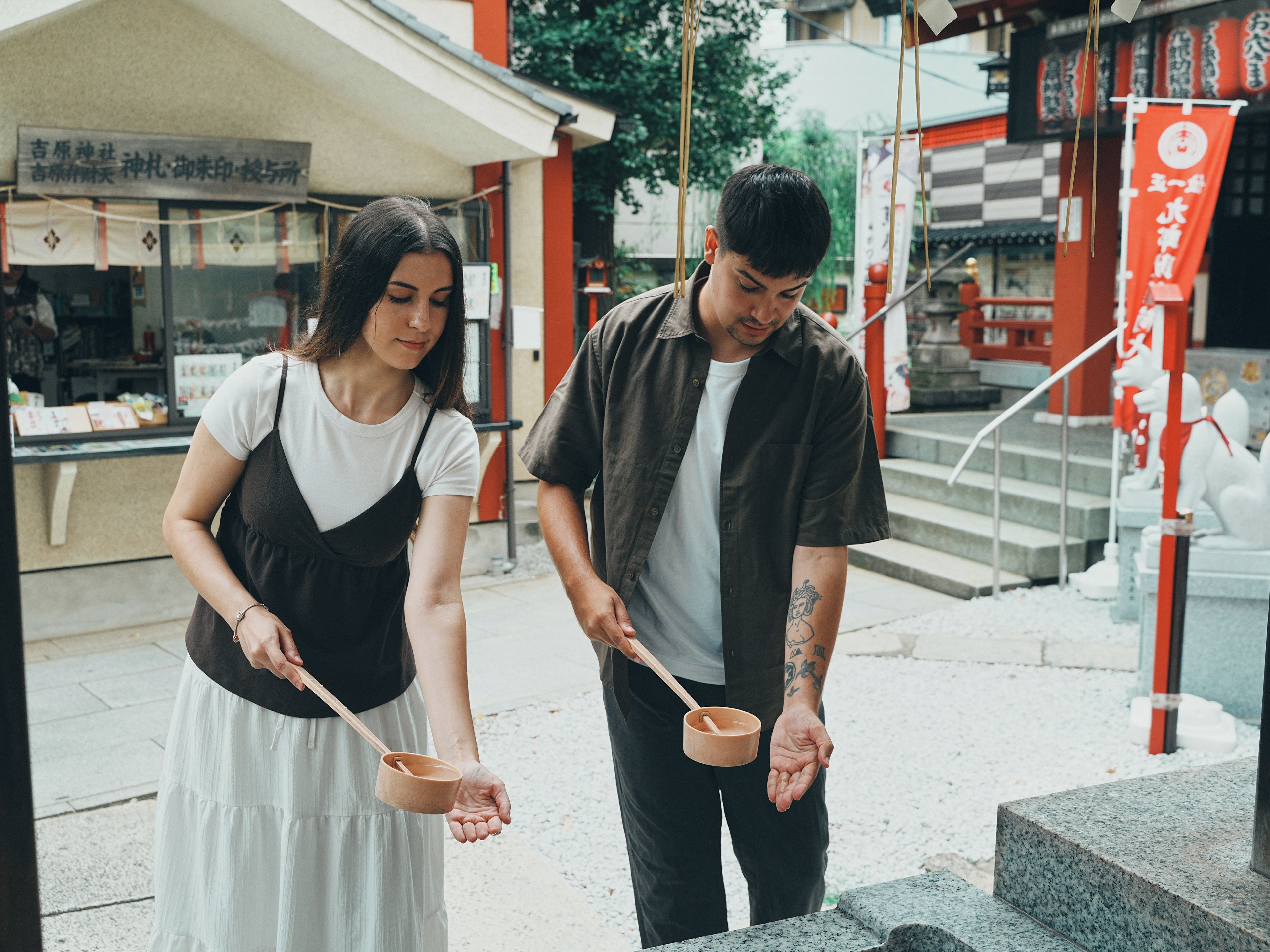 Two individuals holding traditional bowls, standing in front of a building with signage.
