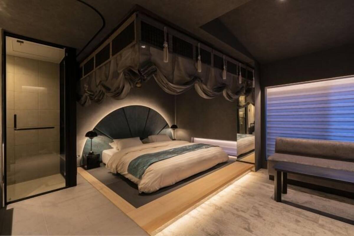 A modern bedroom with a large bed, a bench, and a sliding door.