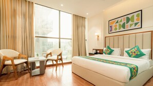 A hotel room with a large bed, two chairs, a small table, a nightstand, and a window with curtains. - Treebo Premium Bizz (Ahmedabad)
